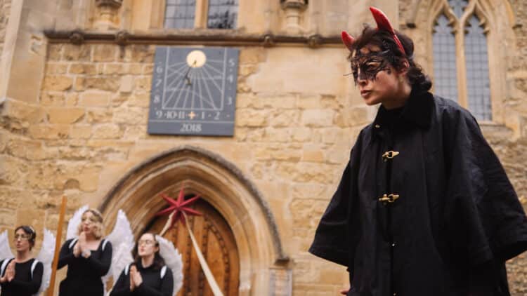 A performer dressed as the devil in front of three angels at the Medieval Mystery Plays